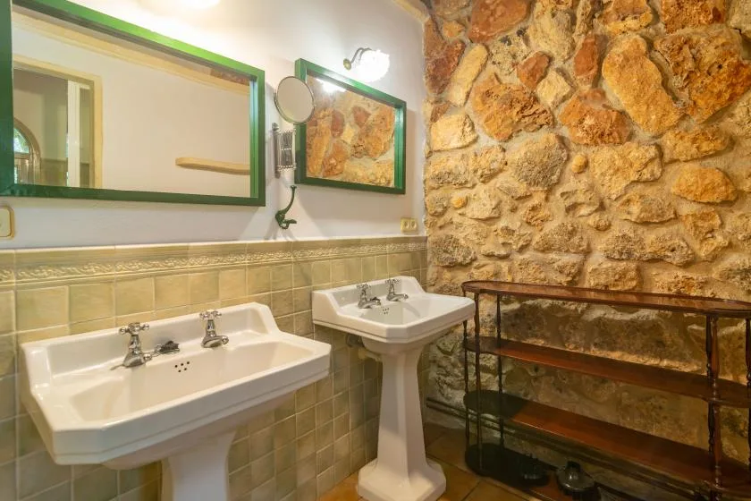 Un baño con dos lavabos de pedestal, paredes de azulejos verdes y una pared de piedra.