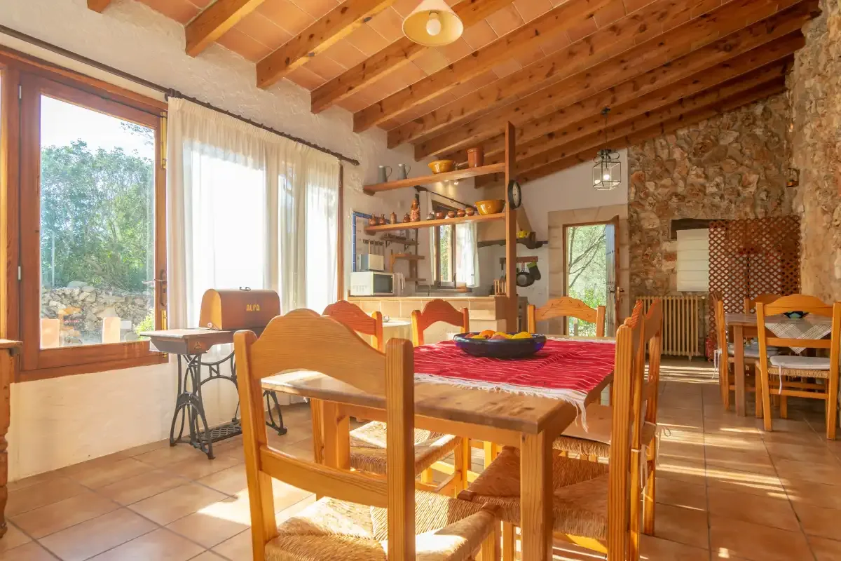 Un comedor con una mesa larga de madera y sillas bajo vigas vistas.
