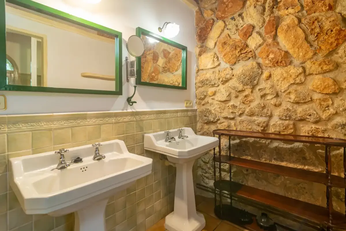 Un baño con lavabos de pedestal, espejos con marco verde y una pared de piedra.