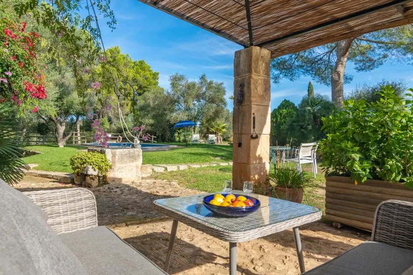 Una zona de estar al aire libre y sombreada da a un jardín con piscina.