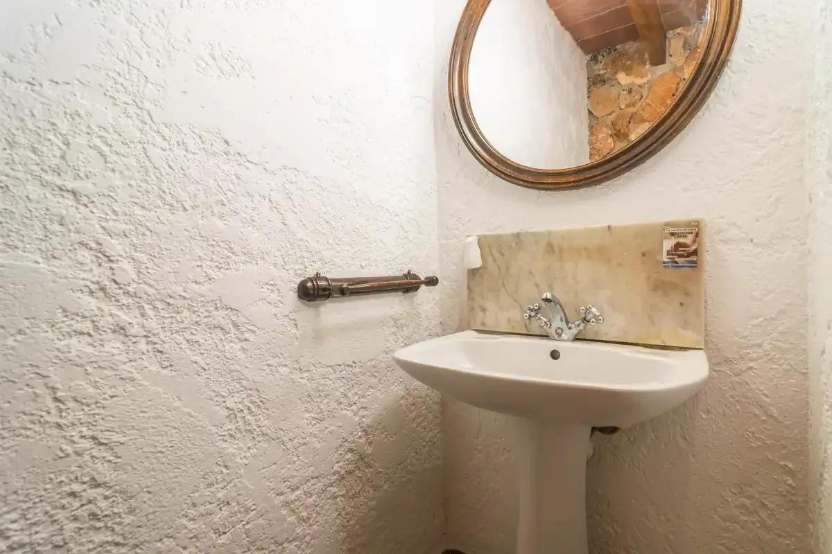Un lavabo de baño está bajo un espejo redondo, junto a paredes con textura.