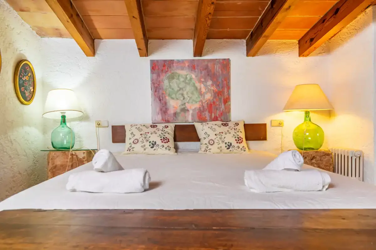 Un dormitorio con una cama grande, toallas dobladas y lámparas junto a la cama bajo vigas de madera vistas.