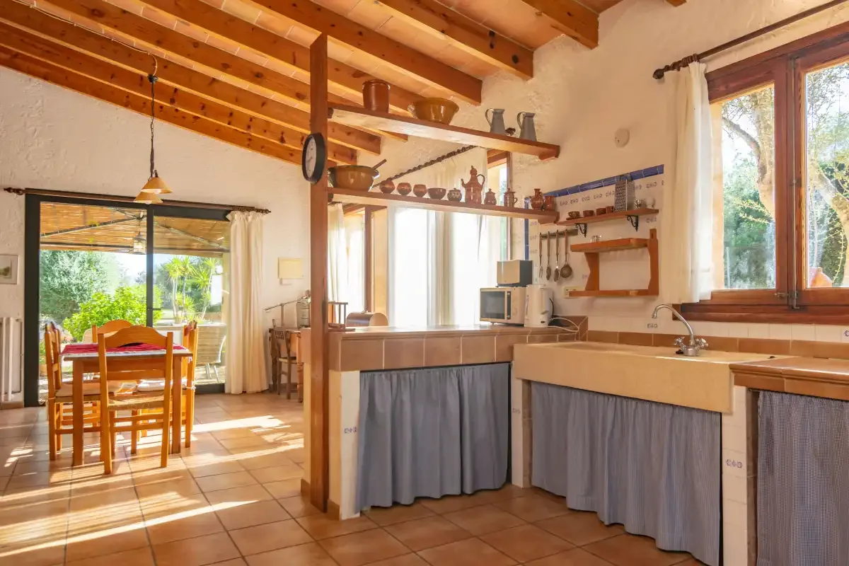 Una cocina y zona de comedor luminosa, con muebles de madera y una mesa junto a las ventanas.