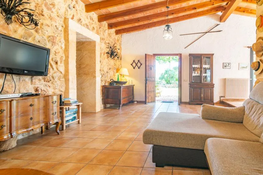 Una sala luminosa con paredes de piedra, vigas de madera a la vista y una puerta abierta.