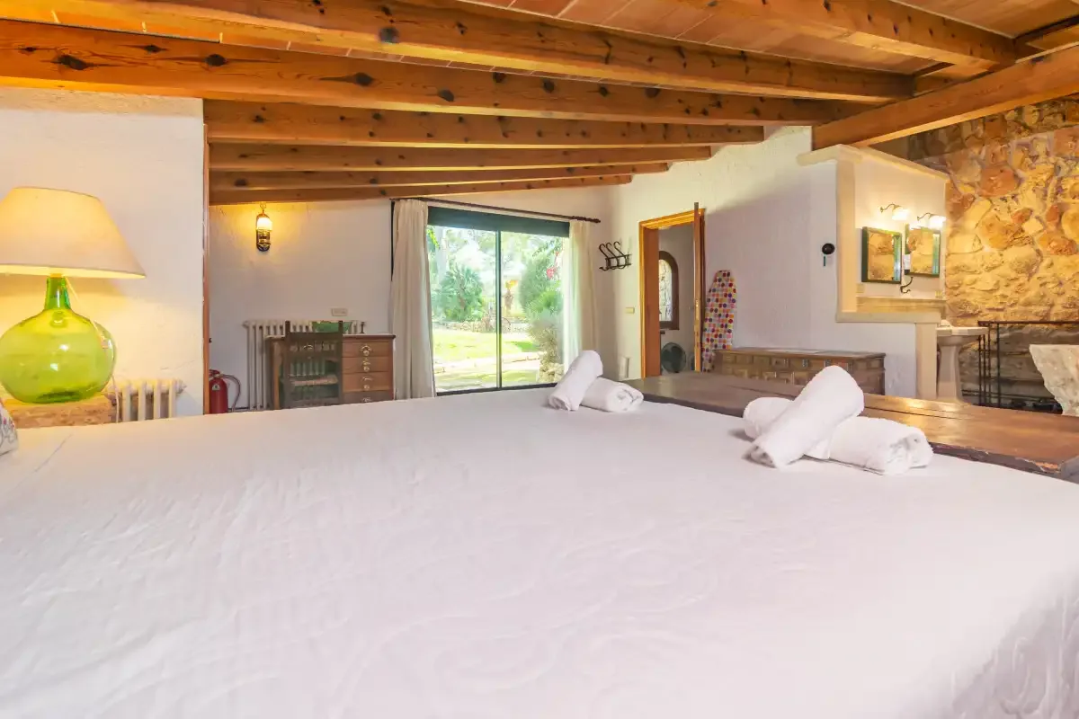 Un dormitorio con una cama grande, vigas de madera vistas y vistas al jardín.
