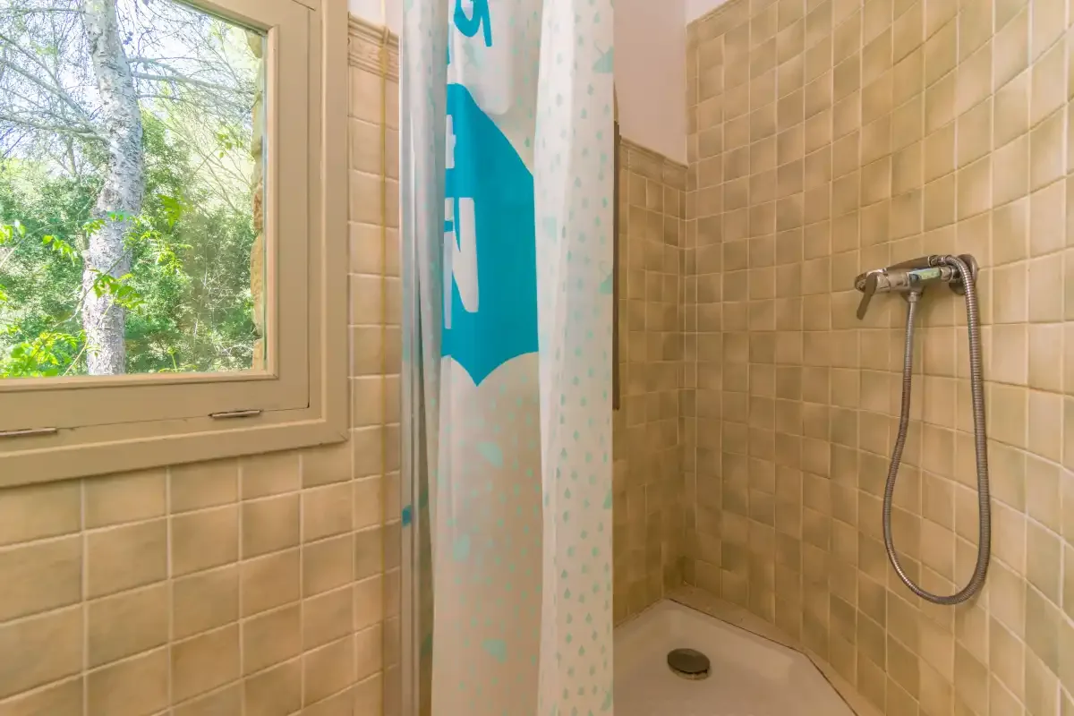 Una ducha de baño con azulejos está junto a una ventana con vistas a la vegetación.