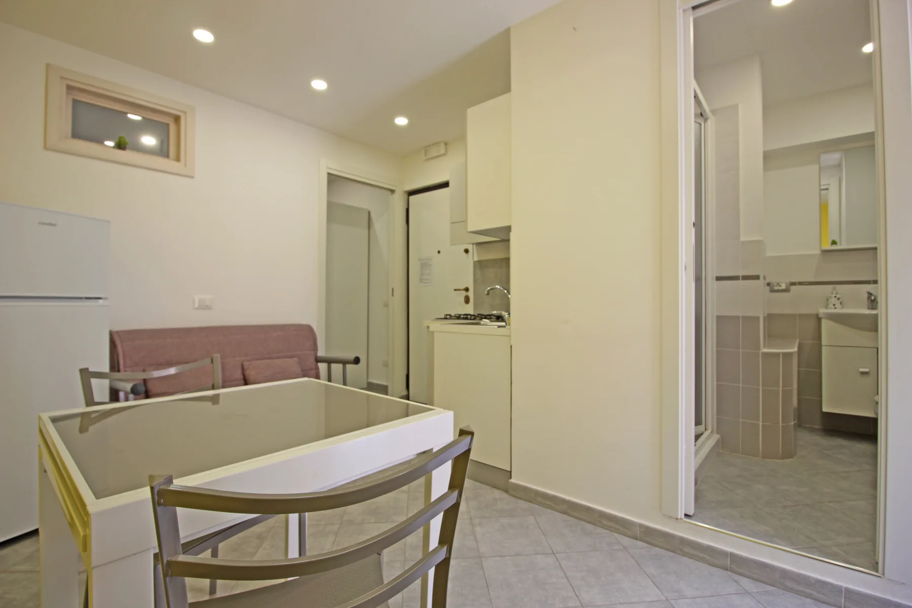 A compact room combines a dining table and seating with a small kitchenette and bathroom.