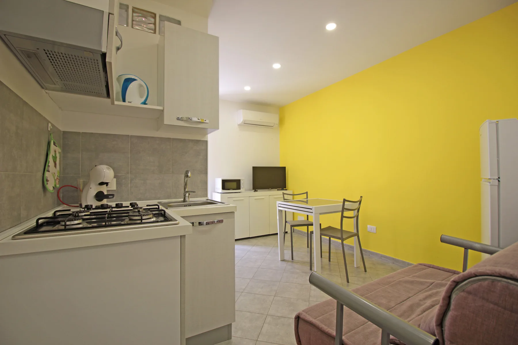 A compact kitchen and dining area with a table beside a bright yellow wall.