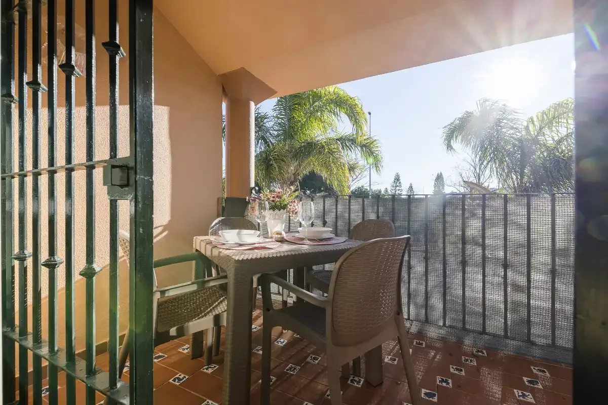 A covered patio has a dining table and seating beside a metal railing.