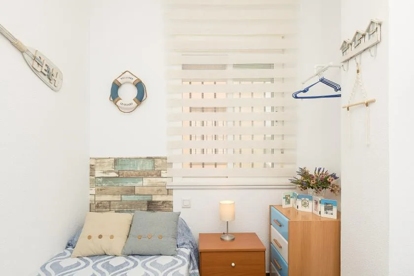 A bright bedroom with a bed, bedside table, and wooden dresser.