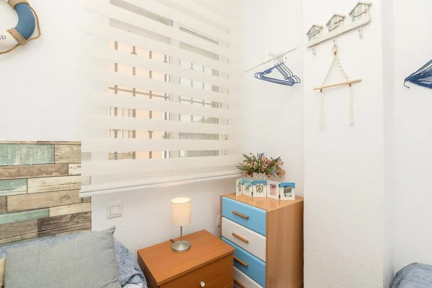 A bright bedroom corner with a bed, bedside table, and colorful drawers.