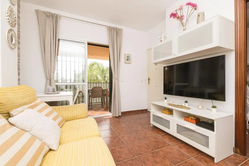 Living room with yellow seating, a wall-mounted television, and a glass balcony door.