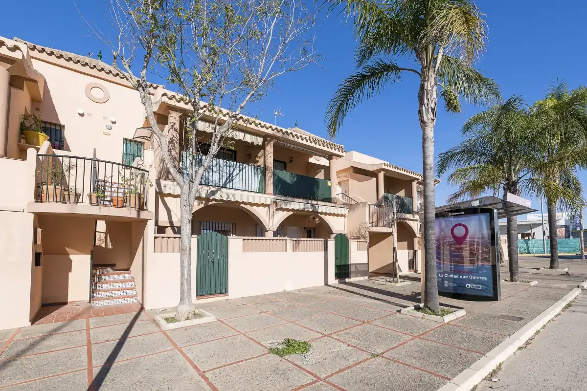 A row of peach-colored buildings with balconies stands beside a paved sidewalk and palm trees.