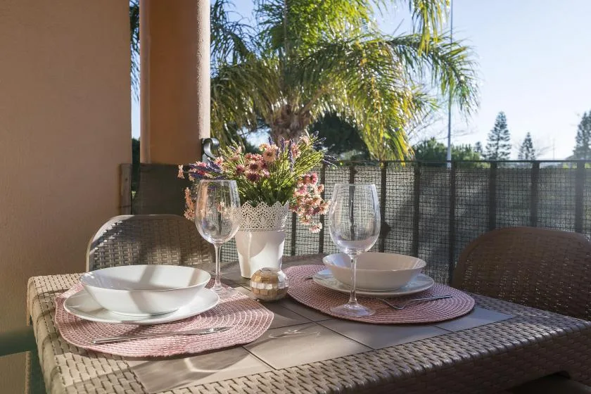 An outdoor dining table is set with plates, glasses, and flowers.