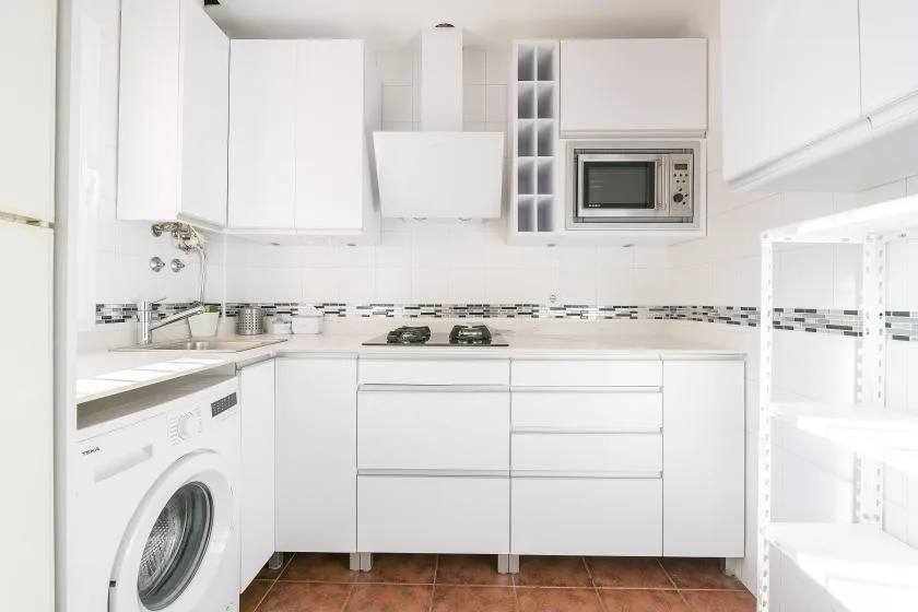 A bright white kitchen with cabinets, a microwave, and a washing machine.