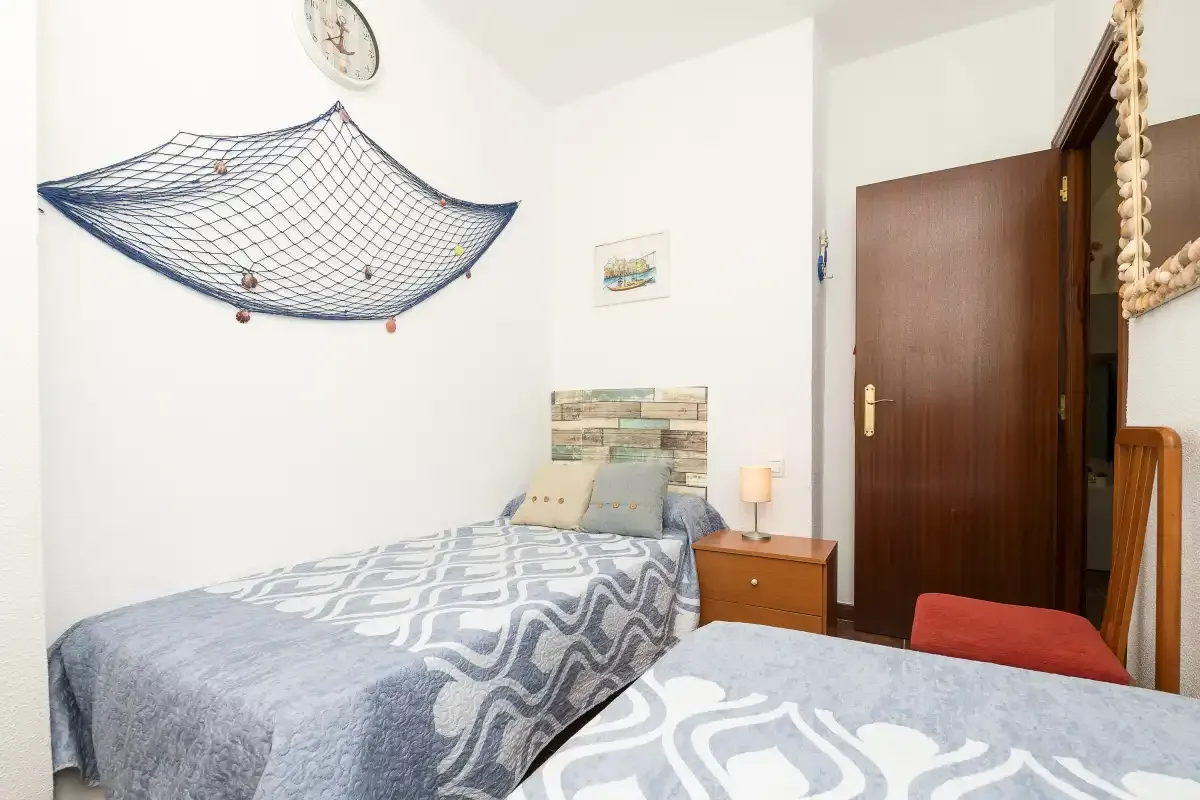 A bedroom with two beds, patterned bedding, and a wooden bedside table.