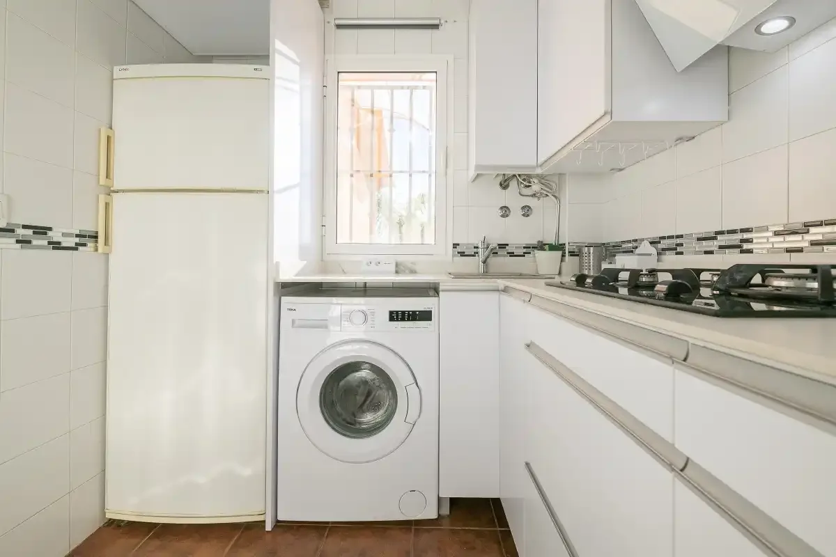 A compact kitchen with a refrigerator, washing machine, and stovetop.