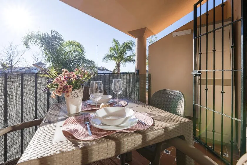A covered outdoor dining area with a set table overlooking palm trees.