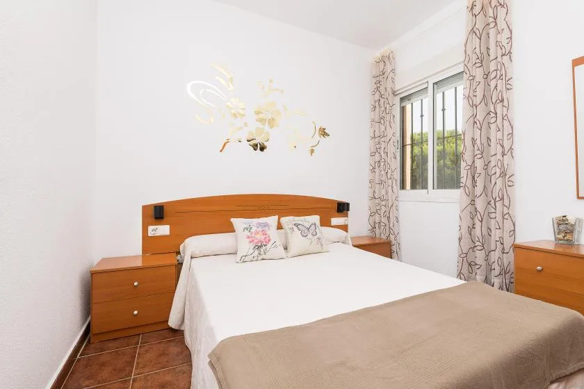 A bright bedroom with a neatly made bed and a window with patterned curtains.