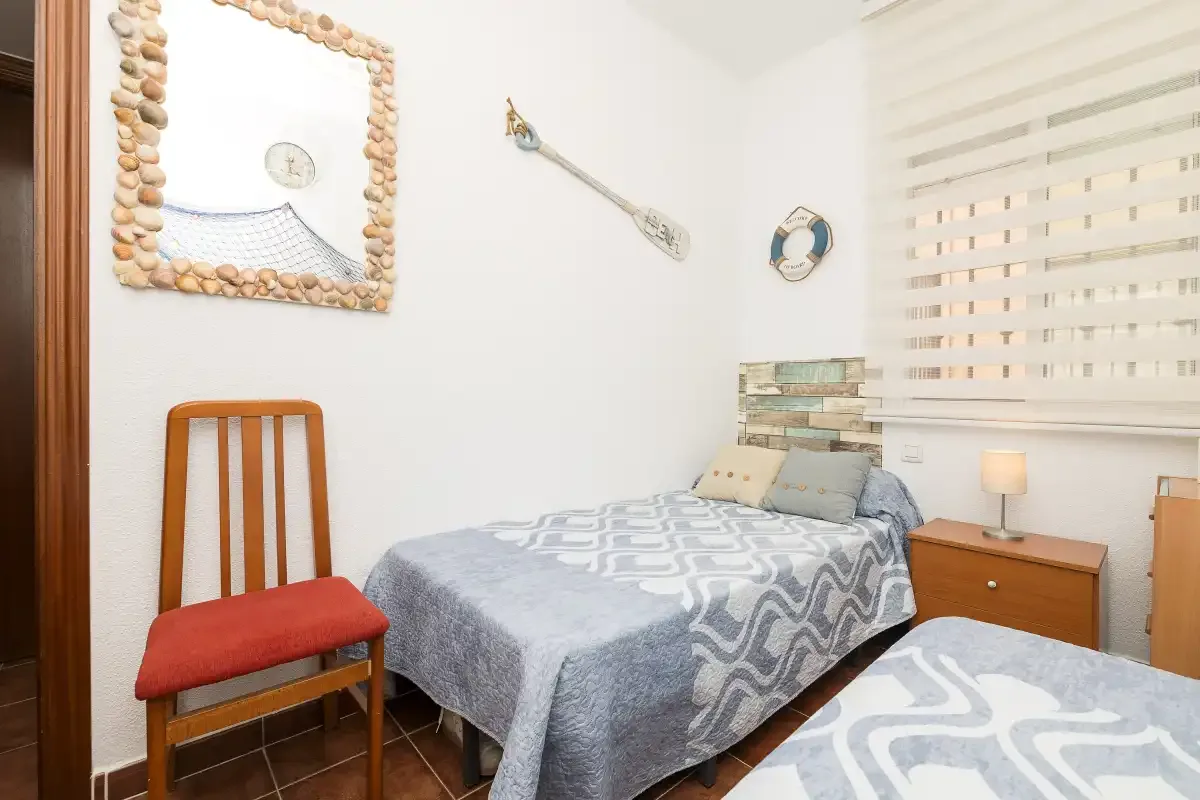A bedroom with two single beds, a chair, and a bedside table.