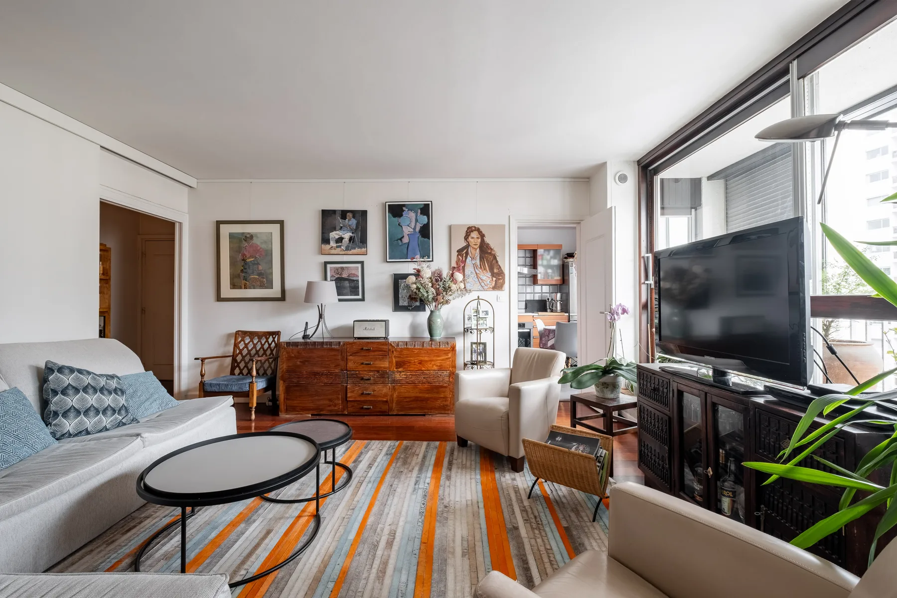 A bright living room with seating, a television, and colorful striped flooring.