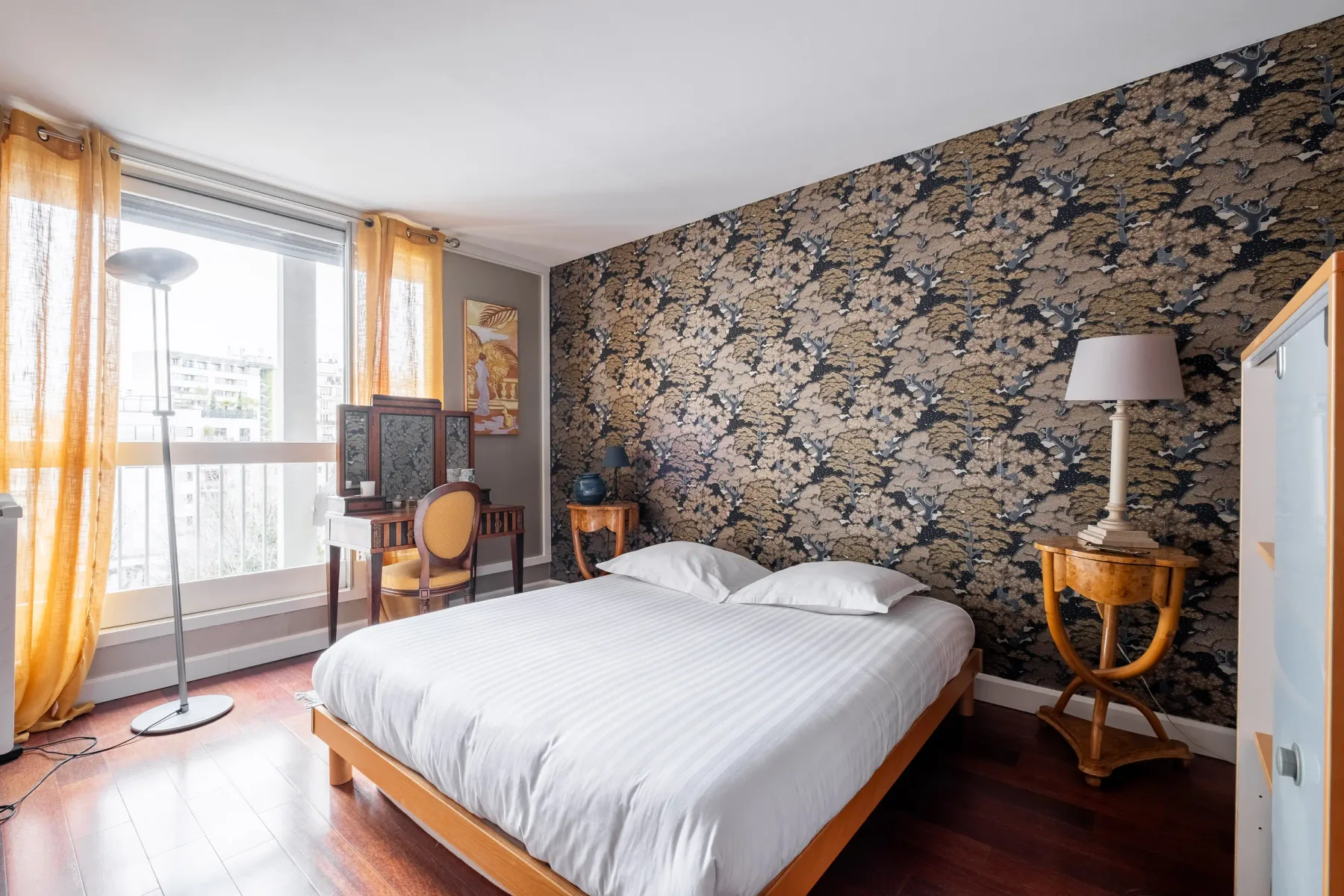 A bedroom with a bed, a floral-patterned wall, and a large window.