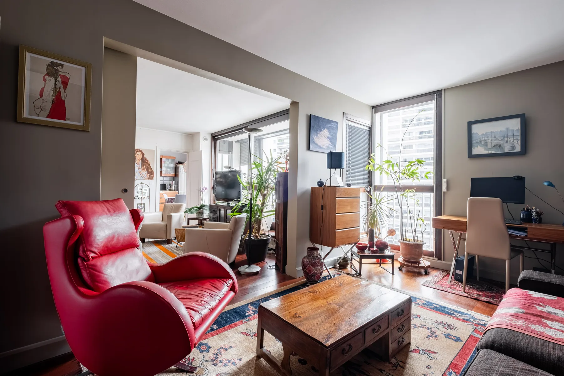 A living room with red seating, a wooden coffee table, and a desk by the windows.