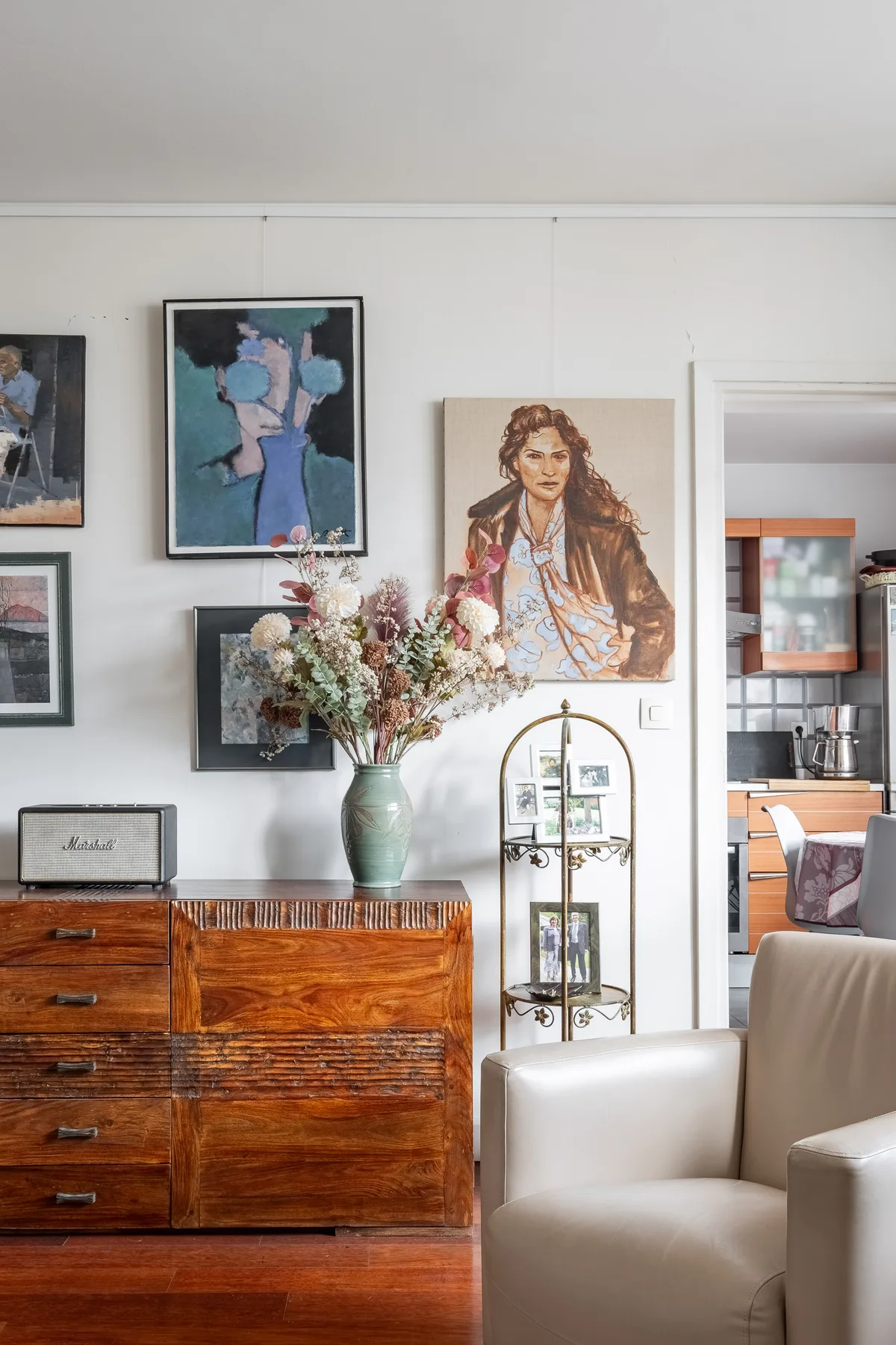A living room with framed artwork, a wooden sideboard, and a vase of flowers.