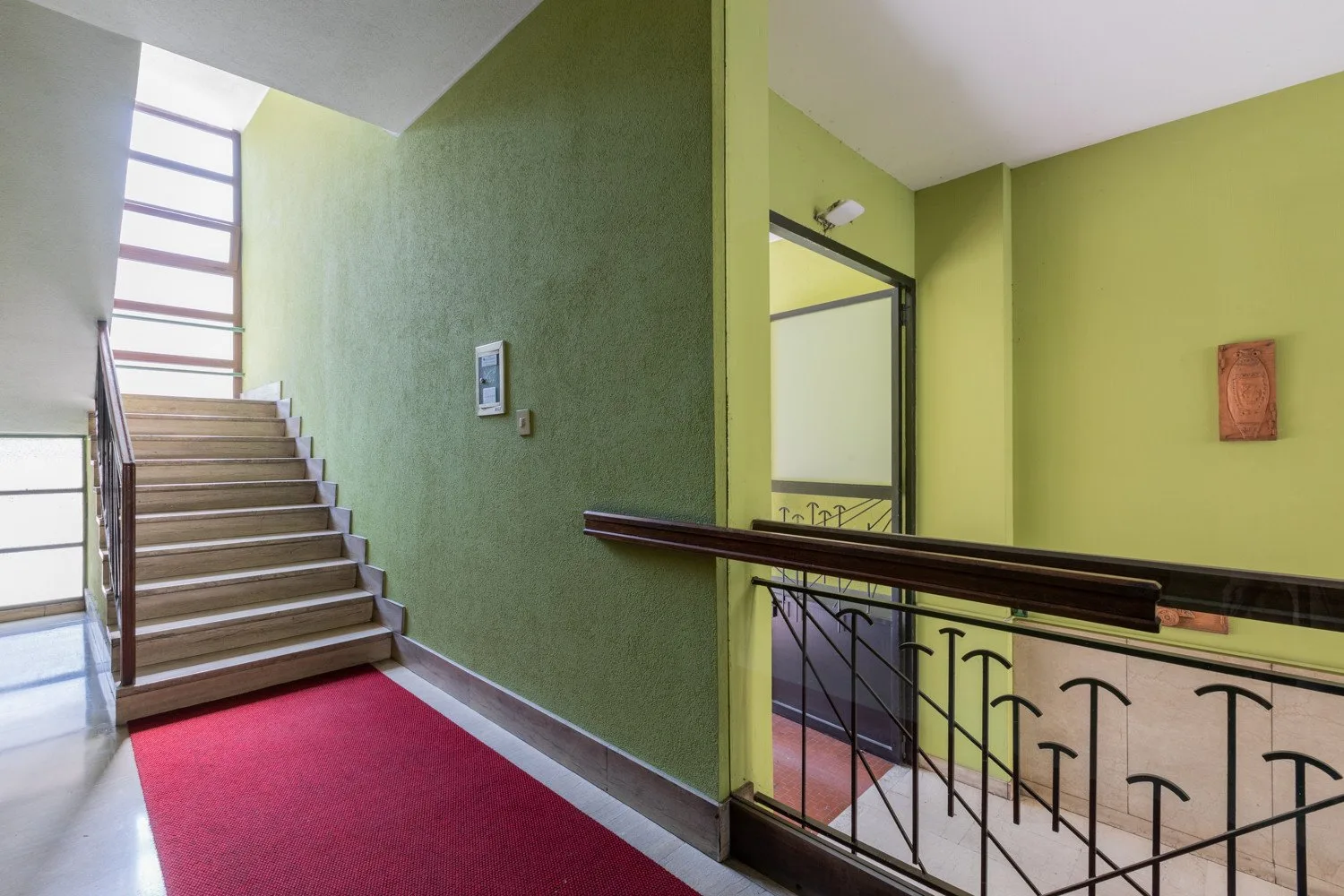 A stairwell with a red carpet runner and a dark metal railing.