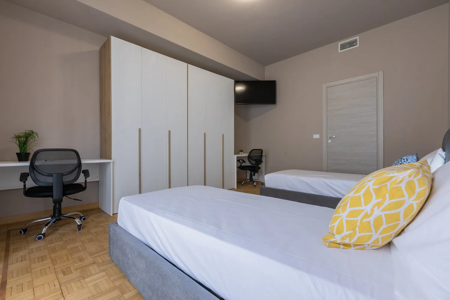 A bedroom with two beds, built-in wardrobes, and a desk.