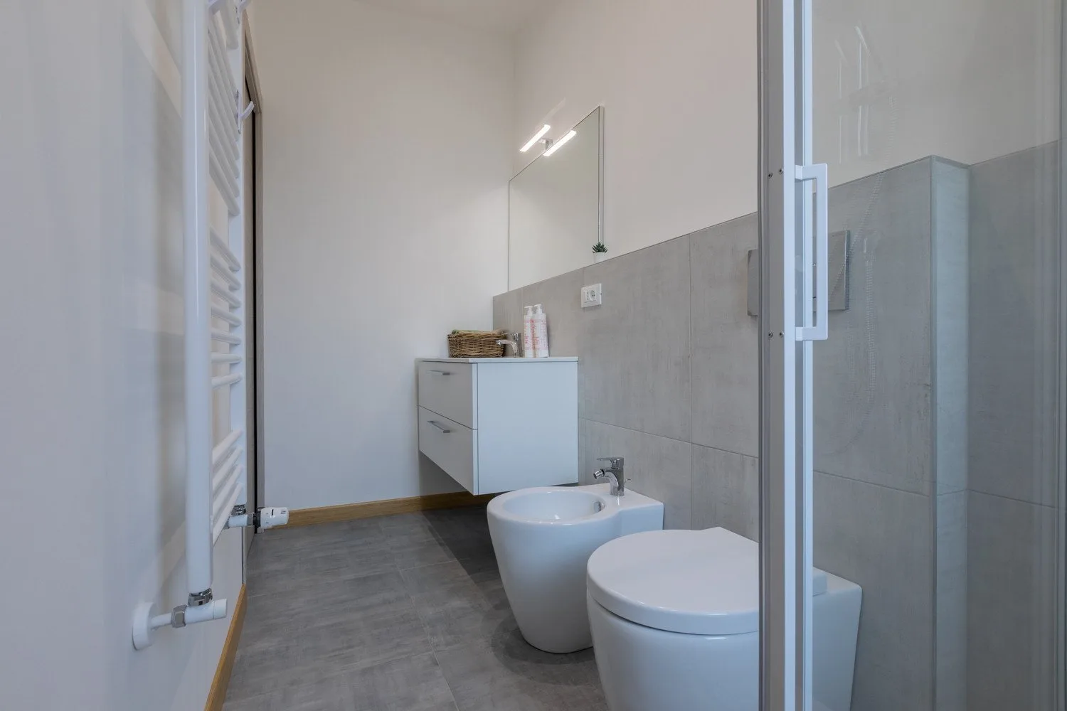 A modern bathroom with a wall-mounted vanity, toilet, bidet, and glass shower.