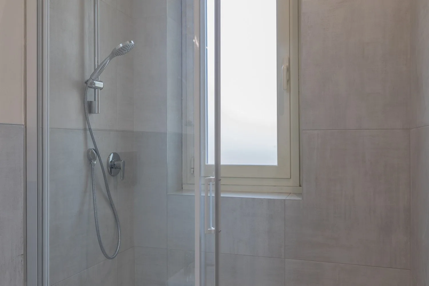 A tiled bathroom shower stands beside a frosted window.
