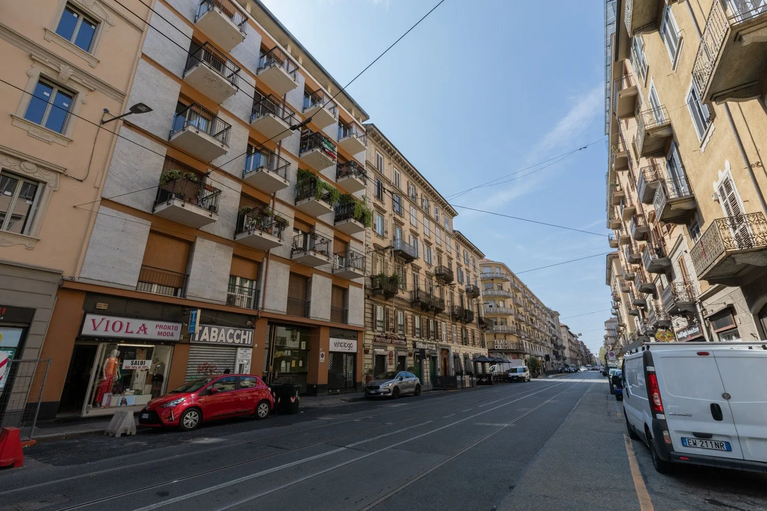 An urban street lined with apartment buildings, storefronts, and parked vehicles.