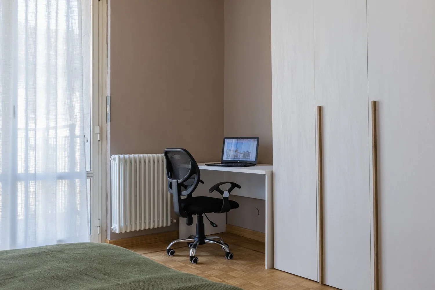 A bedroom with a desk and chair beside a window.