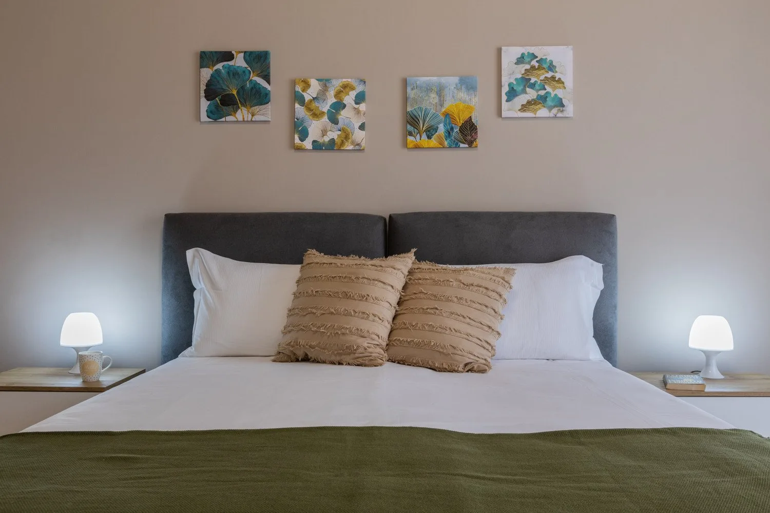 A bedroom with a neatly made bed and floral artwork above the headboard.