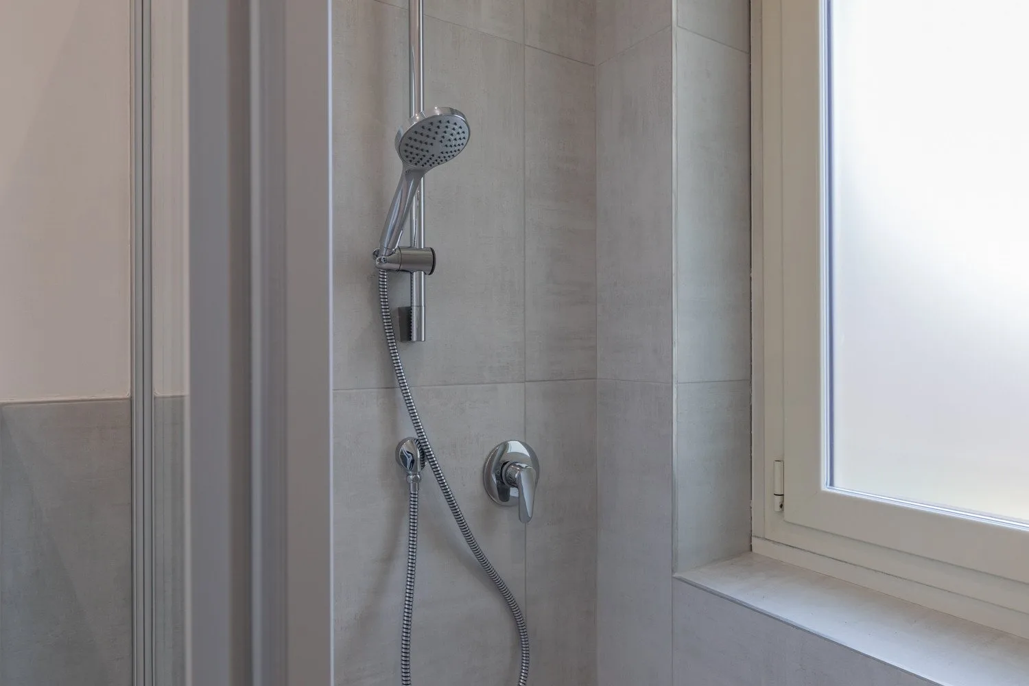 A tiled shower with a handheld showerhead beside a window.