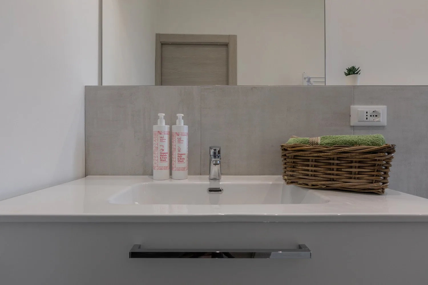 A bathroom vanity with a white sink, soap dispensers, and a woven basket.