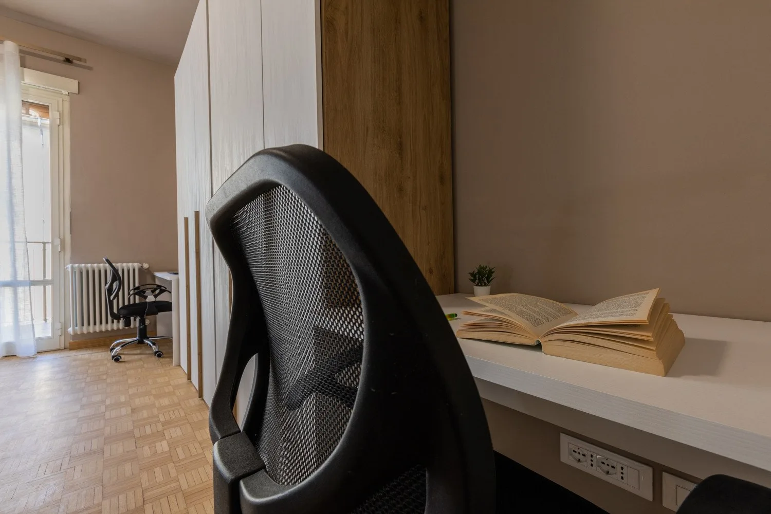 A bright workspace with a desk, office chair, and books beside the window.