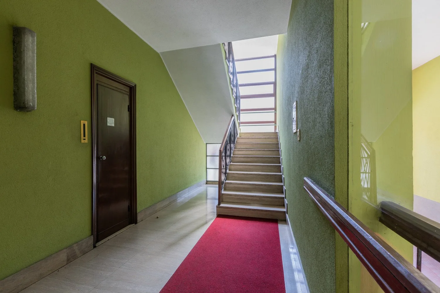 An interior stairwell with a red carpet runner leading up to a landing.