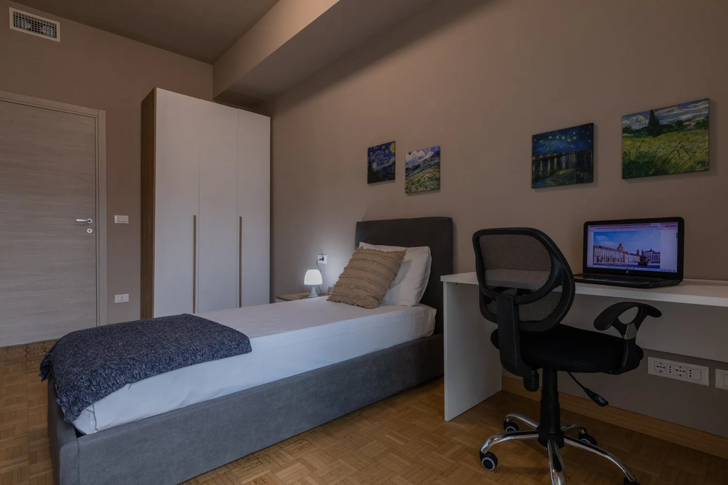 A bedroom with a single bed, wardrobe, and desk with a computer.