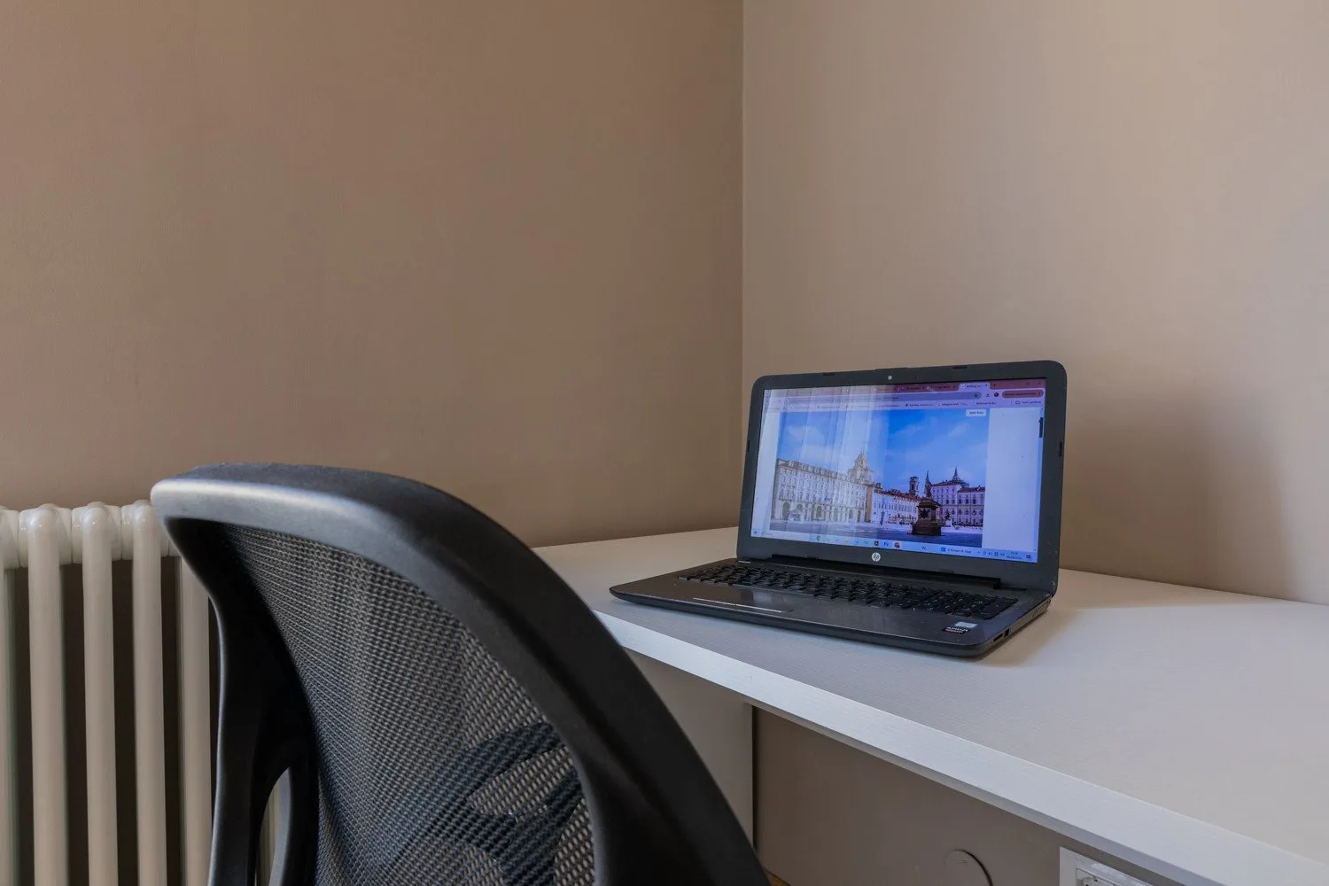 A small workspace with a desk, laptop, and mesh-backed chair.