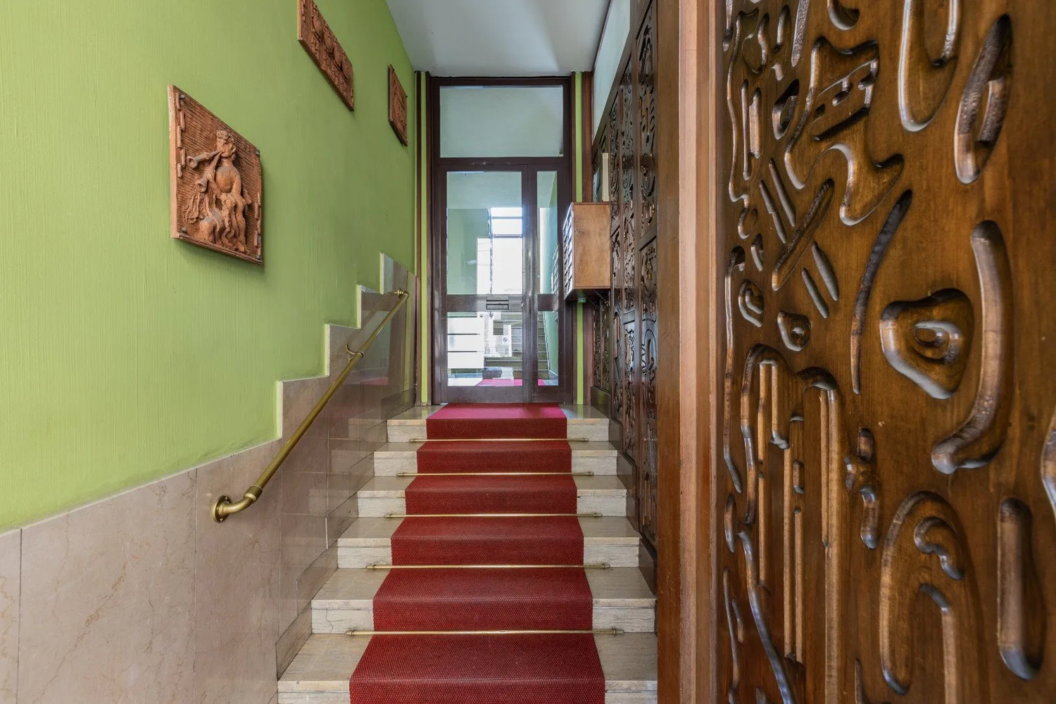 A stairwell with a red runner leads to a glass door.
