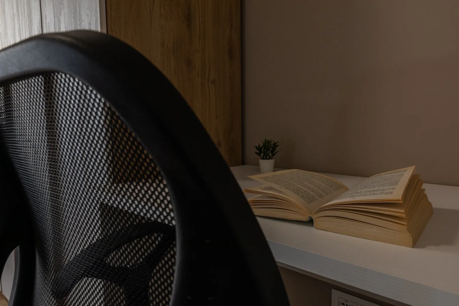 A reading area with an open book on a shelf beside a desk chair.