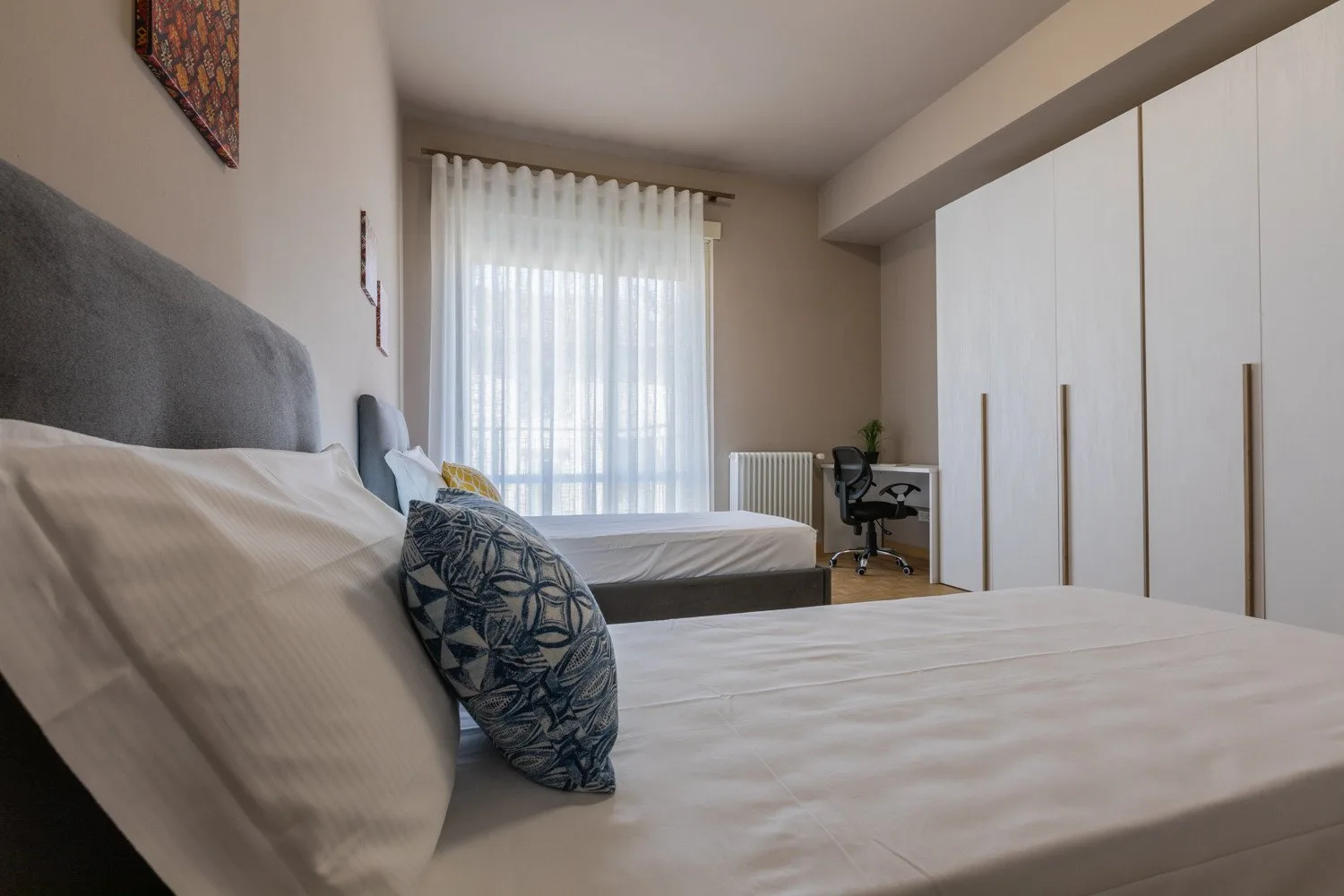 A bedroom with beds, a desk, and a large wardrobe along the wall.
