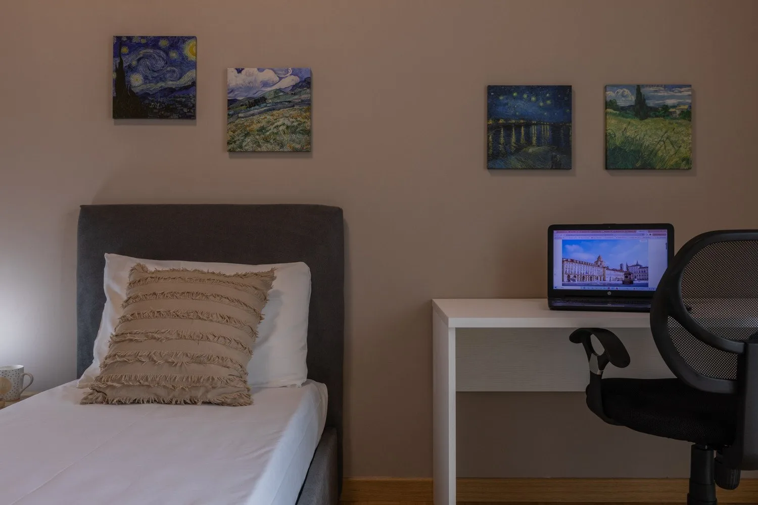 A bedroom with a single bed and a desk beneath framed artwork.
