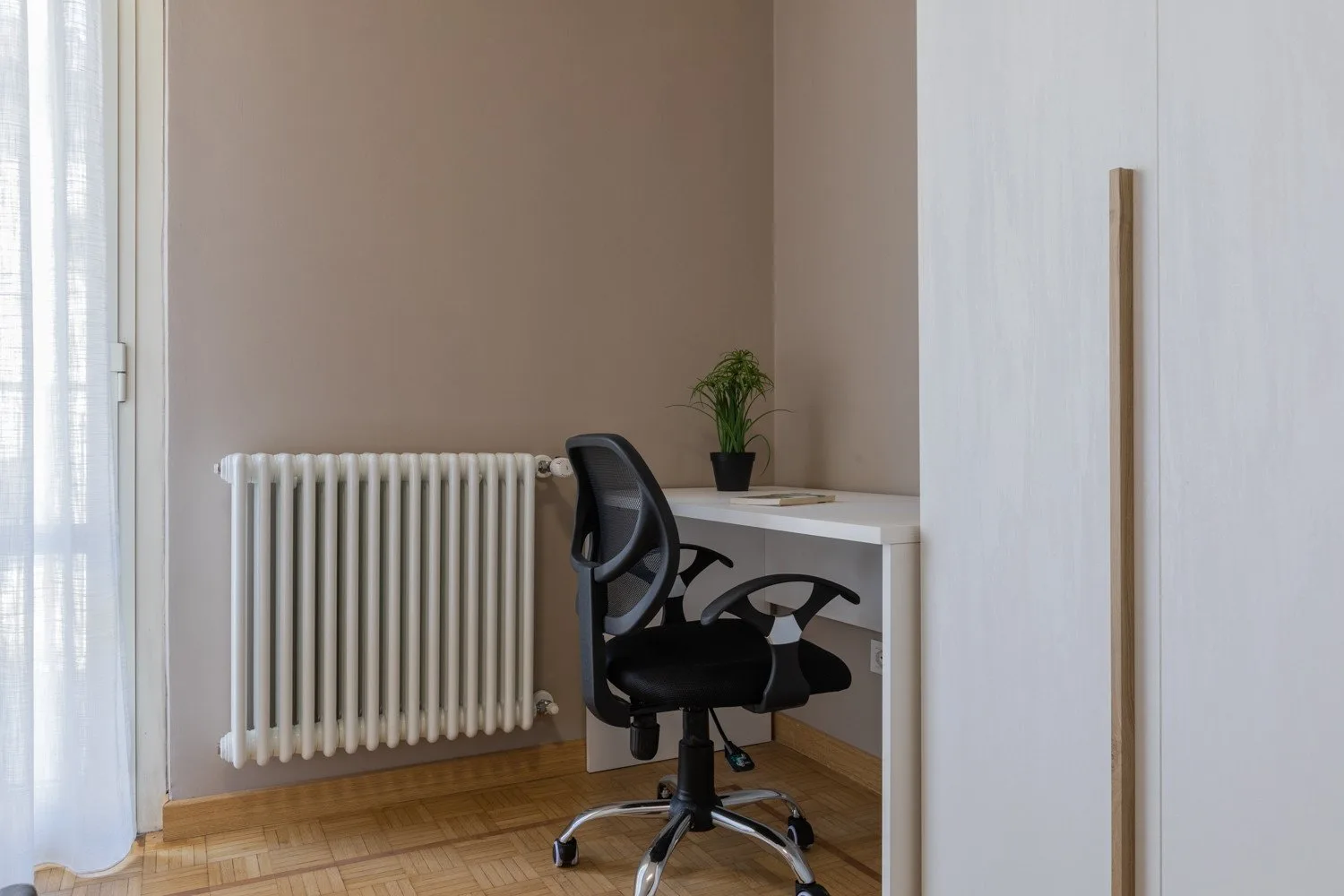 A desk and office chair sit beside a radiator in a bright room.