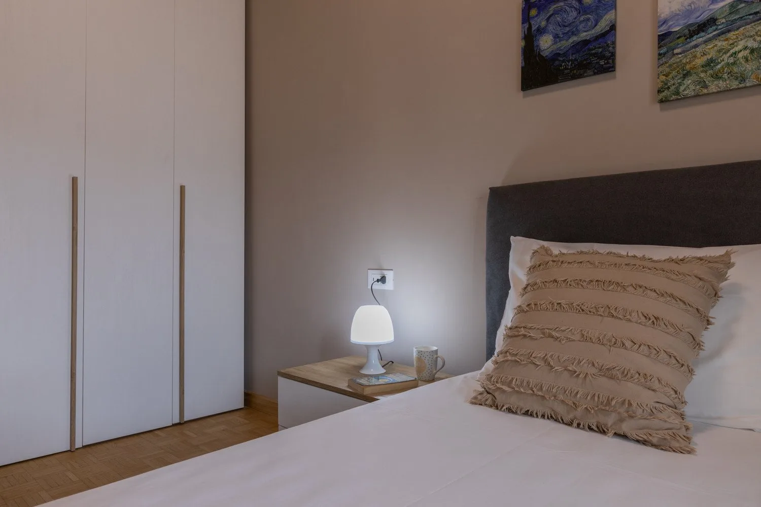 A bedroom with a bed, bedside table, lamp, and white wardrobe.