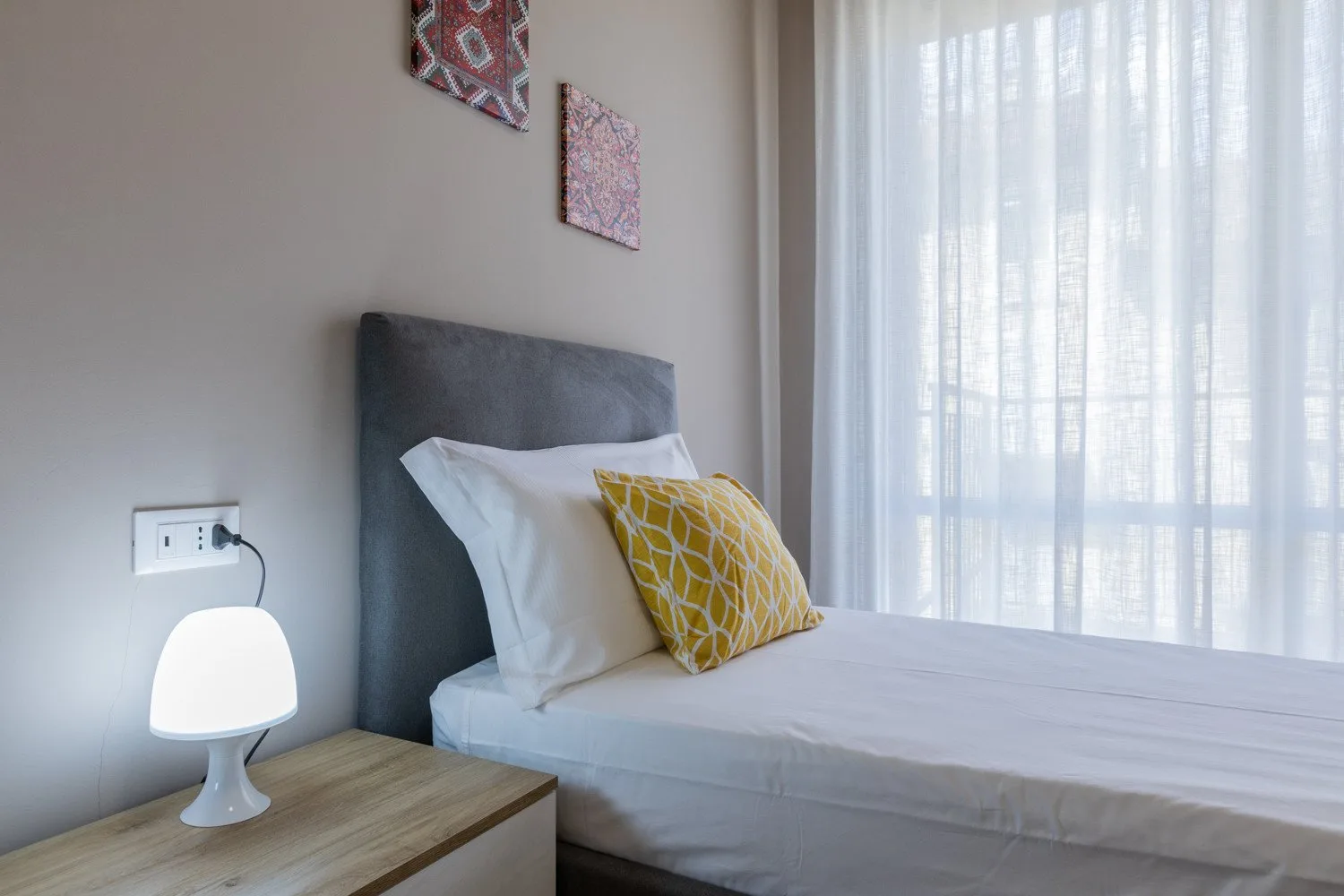 A bedroom with a bed, a bedside table, and sheer curtains.