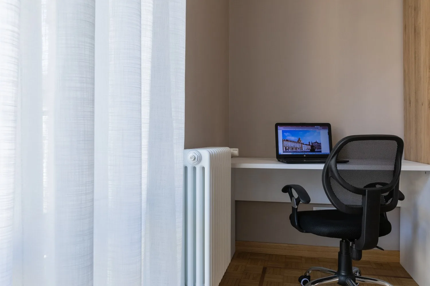 A small workspace with a desk, computer, and office chair beside a curtained window.