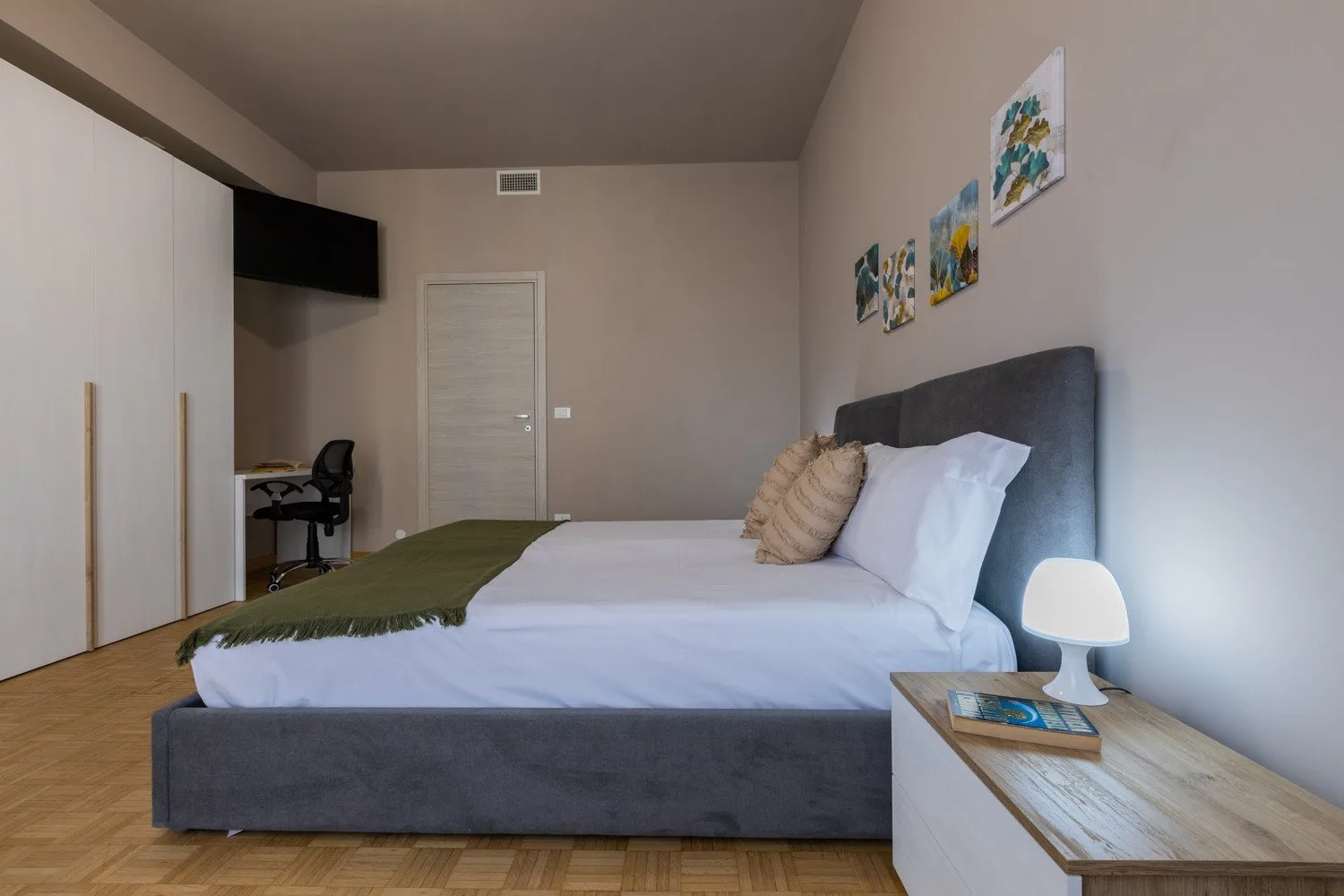 A bedroom with a neatly made bed and framed artwork on the wall.